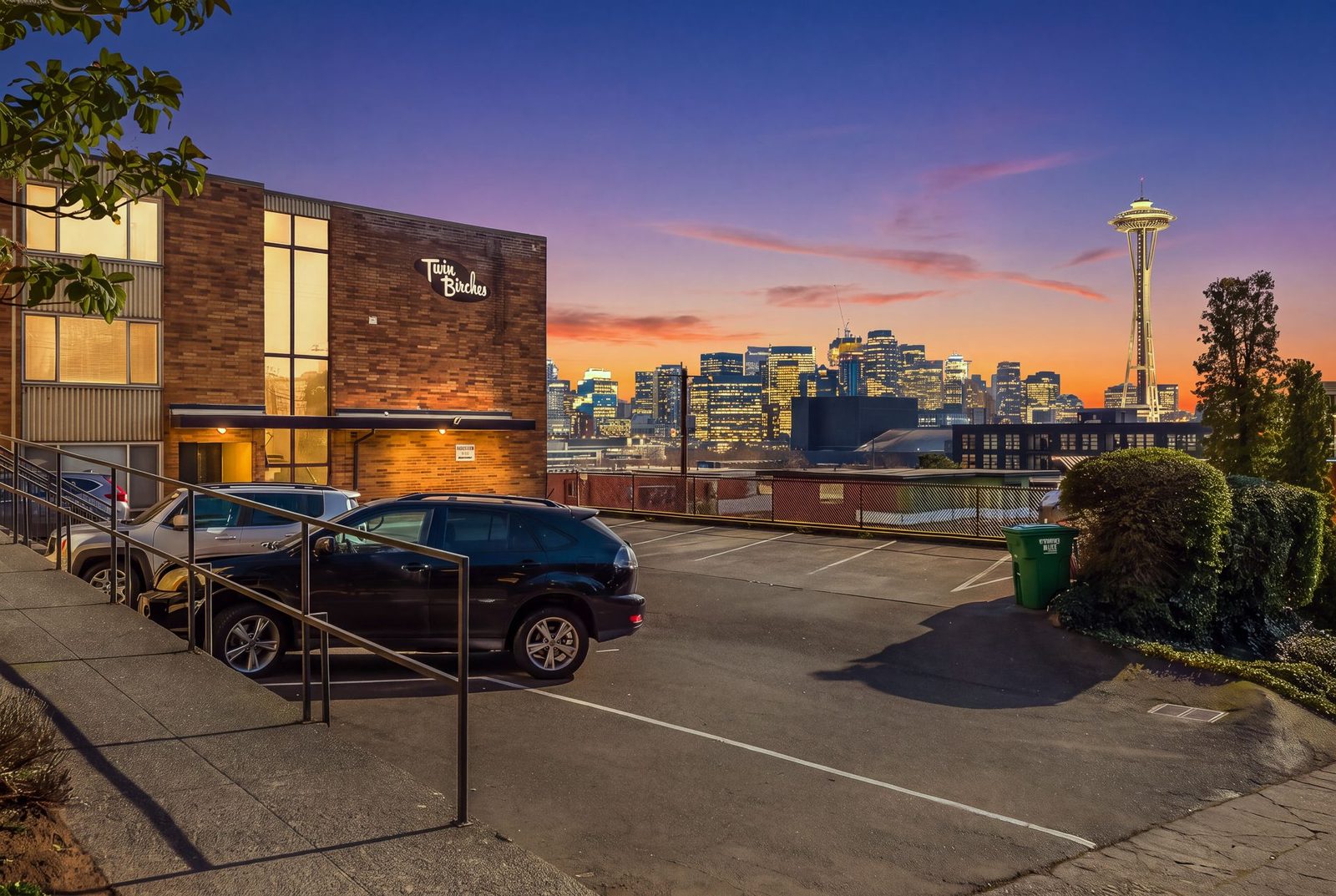 Twin Birches at sunset, its script sign lit on the brick wall, with the downtown Seattle skyline and Space Needle behind
